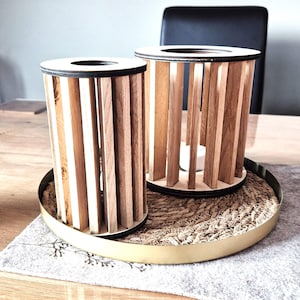 Könnte beinhalten: Zwei Kerzenhalter aus Holz mit einem geflochtenen Sockel und einem goldenen Rand. Die Kerzenhalter sind aus Naturholz mit einer hellbraunen Oberfläche.