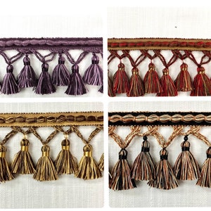 May include: Four samples of tassel trim with different colors and patterns. The trim is made of a woven fabric with a fringe of tassels. The colors are purple, red, gold, and black.
