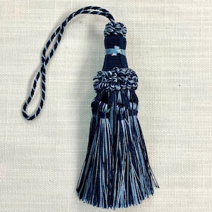 May include: A blue and white tassel with a long cord. The tassel has a layered design with multiple strands of blue and white thread.