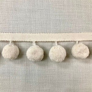 May include: A white pom-pom trim with a white ribbon backing. The trim features a row of fluffy white pom-poms.