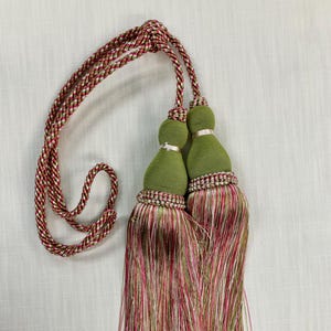 May include: A pair of green tassel tiebacks with a red and white striped cord. The tassels are made of a multi-colored yarn with shades of pink, red, white, and green.