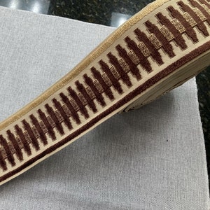 May include: Brown and gold trim with a geometric pattern. The trim is made of a soft, plush fabric.