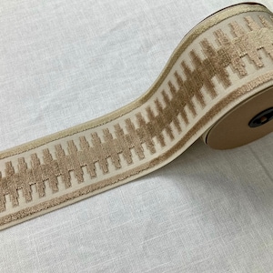 May include: A roll of beige trim with a brown geometric pattern. The trim is woven and has a slightly raised texture.