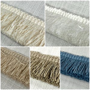 May include: Close-up of decorative fringe trim in five different colors: cream, white, tan, brown, and blue. Each trim features a woven header with long, textured fringe. Ideal for adding a decorative touch to home decor and craft projects.