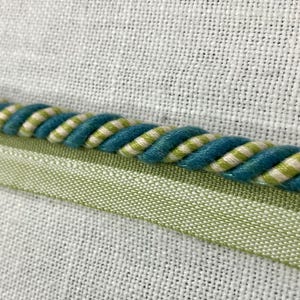 May include: Close-up of a teal and white striped rope trim with a green fabric backing.