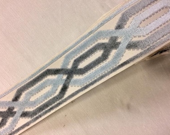 May include: A close-up of a white fabric trim with a repeating geometric pattern in shades of grey and blue. The trim is woven with a raised texture.