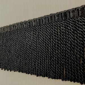 May include: Black fringe trim with a woven texture. The fringe is about 1 inch long.