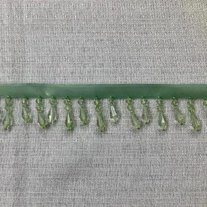 May include: Green beaded trim with a satin ribbon backing. The beads are faceted and have a teardrop shape.