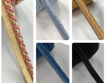 May include: Assortment of braided trim in various colors, including beige, pink, blue, and black. The trim is shown on spools and is ready to be used for sewing and crafting projects.