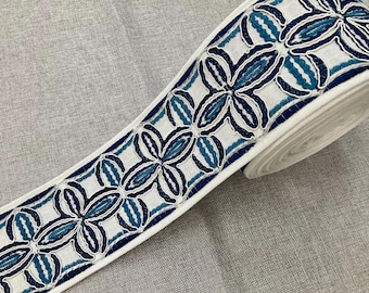May include: White fabric trim with a blue and teal floral pattern. The trim is rolled up and the pattern is visible on the fabric.