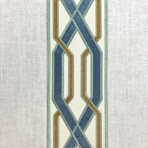 May include: A white fabric with a blue and orange geometric pattern. The pattern is a series of interlocking loops.