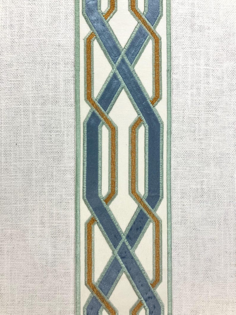 May include: A white fabric with a blue and orange geometric pattern. The pattern is a series of interlocking loops.
