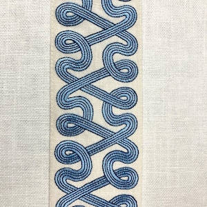 May include: A white fabric with a blue embroidered border. The border is a repeating pattern of interlocked loops.