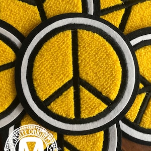 May include: A close-up of several yellow peace sign patches with black and white trim. The patches are made of a fuzzy material and are circular in shape.