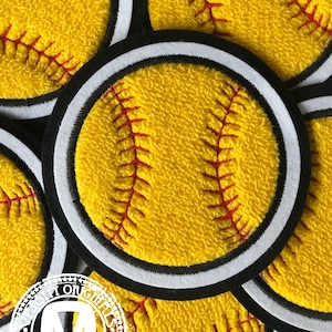 Könnte beinhalten: Nahaufnahme eines gelben Softballs mit roten Nähten, umgeben von anderen Softbällen. Der Softball befindet sich auf einem schwarzen und weißen Stoffpatch.
