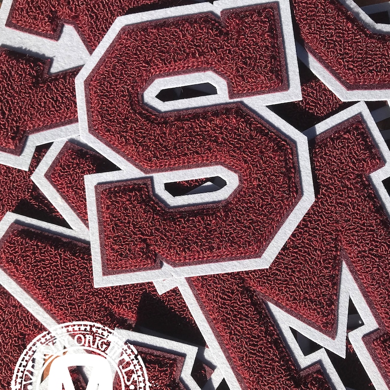 May include: Close-up of maroon chenille letter patches with white borders. The patches are in the shape of the letter "S" and are layered on top of each other. The patches have a textured appearance.