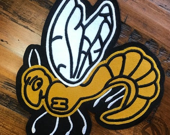 May include: A yellow and black embroidered patch of a cartoon bee with wings. The bee has a number "13" on its body.