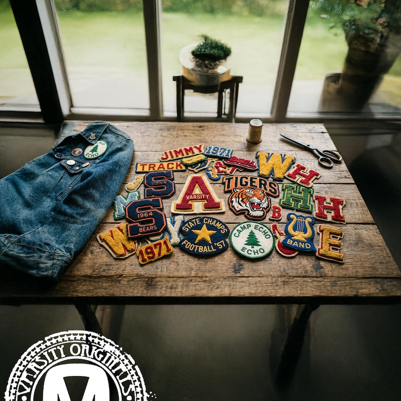 May include: A collection of varsity patches and a denim jacket are arranged on a wooden table. The patches feature various colors, letters, and designs, including a tiger, a star, and the words "Varsity" and "Tigers".