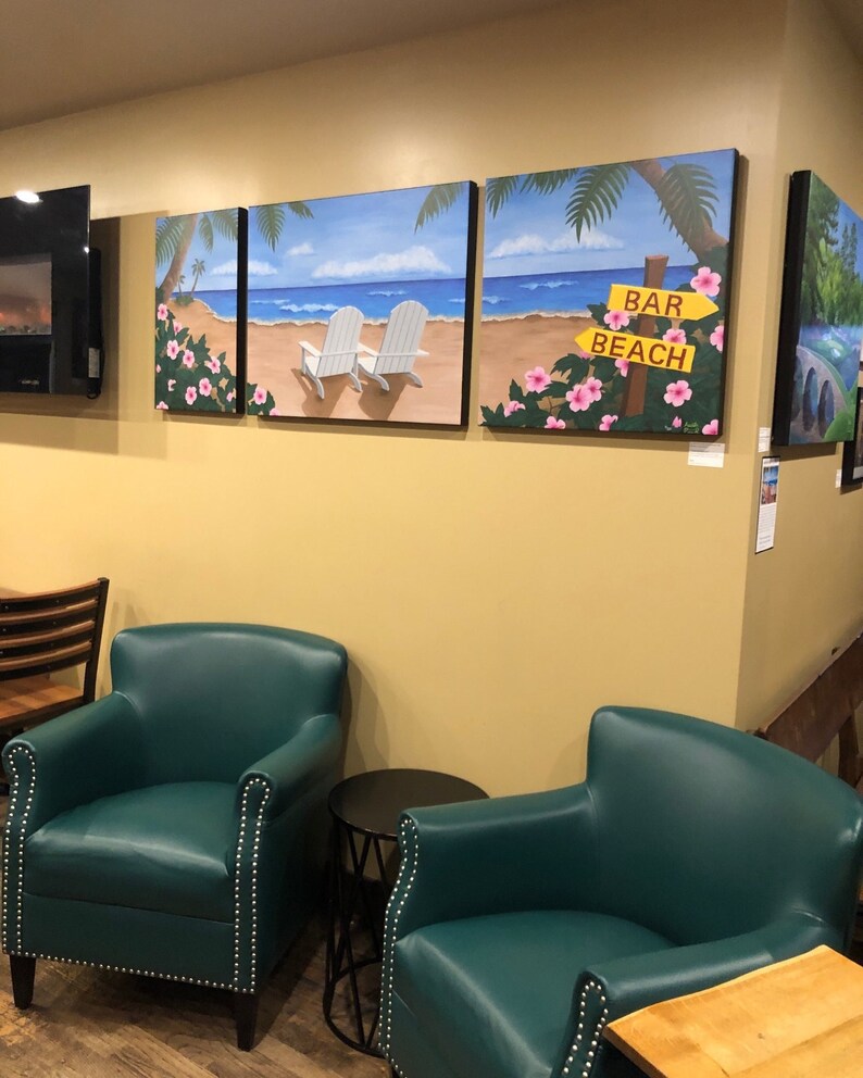 May include: Two teal green armchairs with tufted upholstery and nailhead trim, facing each other in a room with a yellow wall. Three paintings depicting a beach scene with palm trees, white beach chairs, and a sign that reads "Bar Beach" are hanging on the wall.
