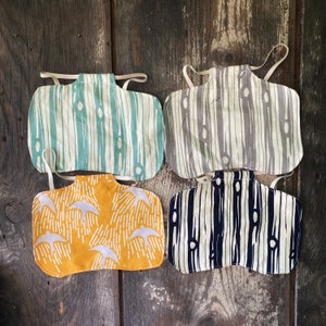 May include: Four fabric bibs with different patterns. The bibs are made of a white fabric with a black, gray, or yellow pattern. The patterns are all geometric and abstract.