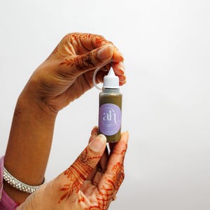 Amarya Henna stained hands holding a small freckles bottle with Amarya Henna purple label against a white background