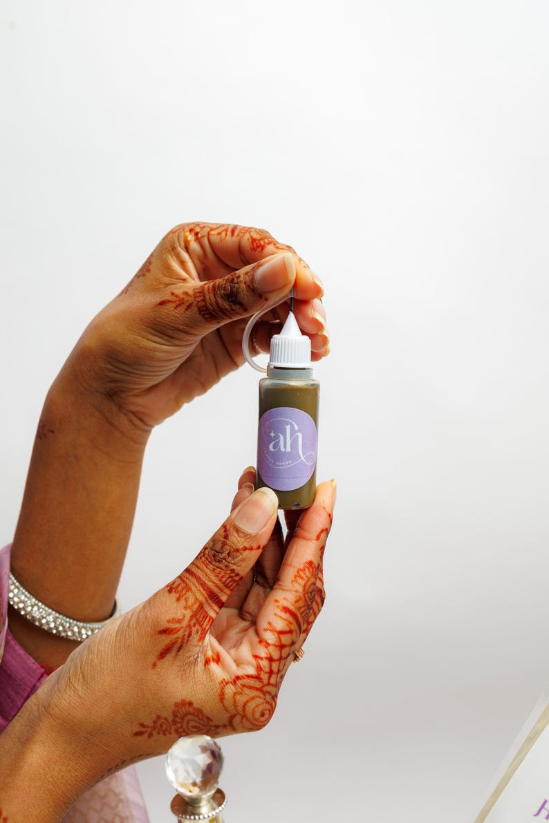Amarya Henna stained hands holding a small freckles bottle with Amarya Henna purple label against a white background