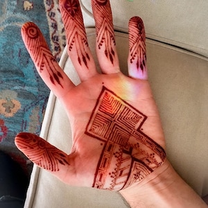Woman hand palm with intricate symmetrical henna designs applied using Amarya Henna cones.