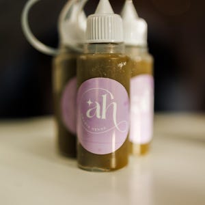 Three small bottles of Amarya Henna freckle bottles with a purple label featuring 'ah' logo on a blurred background