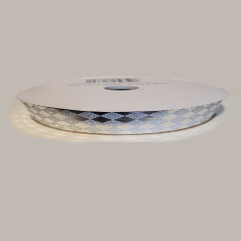 Pu&ograve; includere: Una bobina di nastro con un motivo ripetuto a rombi argento e bianchi con una finitura glitterata. Il nastro &egrave; avvolto attorno a un nucleo di cartone circolare bianco, mostrando un design geometrico coerente lungo il bordo esterno.