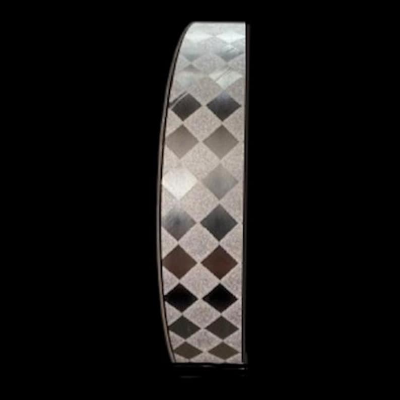 Pu&ograve; includere: Un oggetto verticale curvo caratterizzato da un motivo a rombi ripetuto in tonalit&agrave; alternate di argento, grigio e antracite scuro. La superficie ha un aspetto metallico testurizzato con una forma ad arco distinta, su uno sfondo nero.