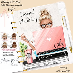 K&ouml;nnte beinhalten: Ein wei&szlig;er Planer mit einer goldenen Spiralbindung. Der Umschlag zeigt eine digitale Illustration einer Frau mit blonden Haaren, die eine Brille und ein blaues Hemd tr&auml;gt. Sie sitzt an einem Schreibtisch mit einem Laptop, auf dem "Beauty" steht, und einer Kaffeetasse, auf der "Starbucks" steht. Der Text "Focused and Flourishing" befindet sich oben auf dem Planer. Der Text "Lola" befindet sich auf dem Laptop-Bildschirm. Der Text "Watermarks will be removed" befindet sich unten auf dem Planer.