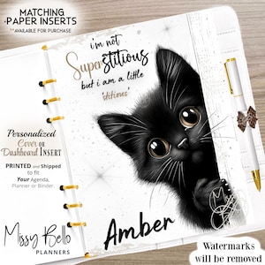 May include: A black cat with big brown eyes peeks out from behind a white planner cover. The planner has gold rings and the text "I'm not superstitious, but I am a little 'stitious'" is written on the cover. The name "Amber" is written below the cat. The text "Personalized Cover or Dashboard Insert" is on the left side of the planner.