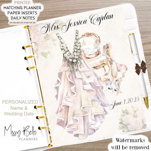 May include: A white planner with a floral design and a watercolor illustration of a wedding dress and a chair. The planner is personalized with the text "Mrs. Jessica Caplan" and "June 1, 2025".