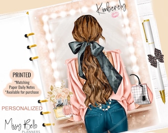 May include: A white planner with a printed illustration of a woman in a pink blouse and blue jeans. The planner includes a pen with a bow, and the text "Kimberly" and "Missy Bello Planners". The planner is personalized and printed.