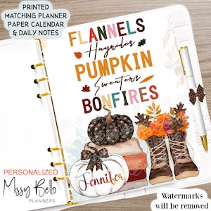 Op de afbeelding: Een witte plannerhoes met een herfstthema met pompoenen, laarzen en bladeren. De tekst "FLANNELS Hayrides PUMPKIN Sweaters BONFIRES" staat in kleurrijke letters. De planner is gepersonaliseerd met de naam "Jennifer".