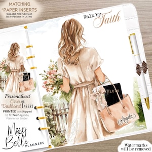 May include: A planner cover featuring a watercolour illustration of a woman carrying flowers and a tote bag with the name "Angela". The words "Walk by Faith" are written at the top. A pen with a bow is on the right. The planner is white.