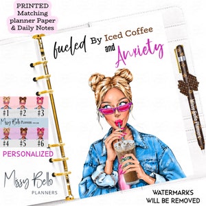 Op de afbeelding: Een witte plannerhoes met een gouden ringband. De hoes heeft een cartoonillustratie van een vrouw met blond haar, die een zonnebril en een spijkerjack draagt. Ze drinkt ijskoffie met een rietje. De tekst "fueled by iced coffee and anxiety" is geschreven in zwarte en paarse tekst.