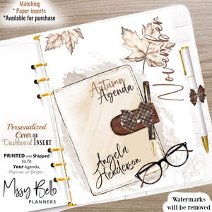 May include: A white planner with gold accents, featuring an "Autumn Agenda" design. Includes a pen, glasses, and decorative leaves. The planner is personalized with a name and the text "November".