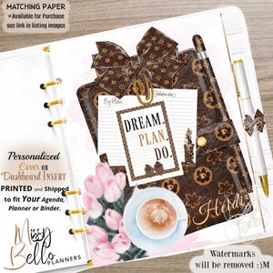 Può includere: Un inserto per agenda con copertina a motivo marrone e un grande fiocco, un blocco note bianco con il testo DREAM. PLAN. DO., una tazza di caffè e tulipani rosa. Una penna bianca con un piccolo fiocco è fissata sul lato dell'agenda.