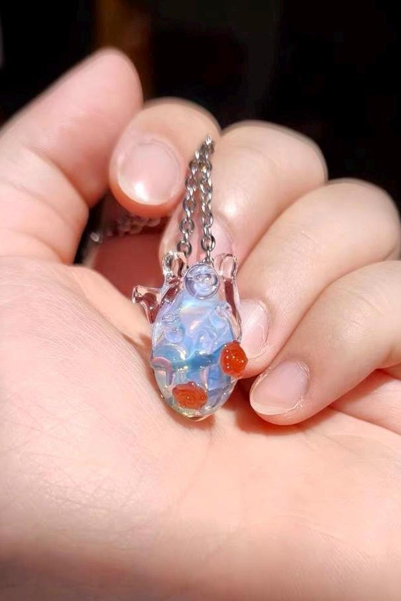 May include: A delicate silver chain necklace with a glass pendant featuring a blue and iridescent design. The pendant has red glass roses attached to it.