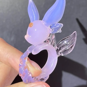 May include: A small glass figurine of a purple and blue seahorse with a curled tail. The seahorse has a pink eye and a clear glass fin.