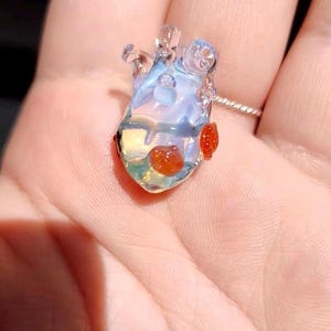 May include: A clear glass heart pendant with red glass accents. The pendant is iridescent and has a delicate, intricate design.