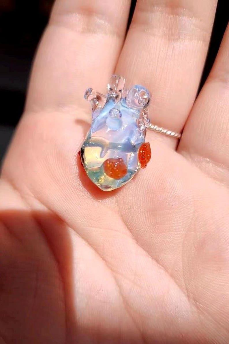 May include: A clear glass heart pendant with red glass accents. The pendant is iridescent and has a delicate, intricate design.