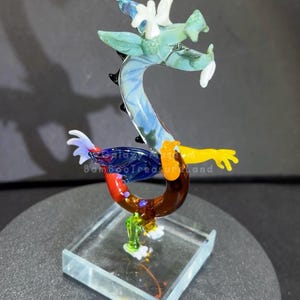 May include: A colorful glass dragon figurine. The dragon features a blue, green, yellow, red, and brown body with white accents. It is mounted on a clear, square base. The text "galaxy BambooTreasureland" is visible on the dragon.