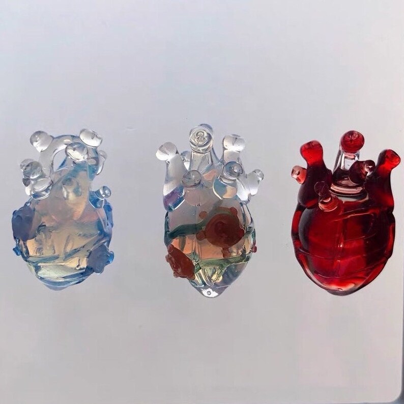 May include: Three glass heart ornaments, one is clear with iridescent blue, one is clear with green and red, and one is red.