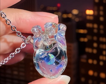 May include: A clear glass heart necklace with a iridescent opal inside. The heart is detailed with a textured surface and a silver chain.