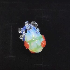 May include: A small glass heart charm with red and blue accents. The heart is translucent and has a green swirl inside.