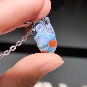 May include: A delicate glass pendant necklace with a clear, iridescent, teardrop-shaped charm. The charm has small, red, glass beads embedded in it.