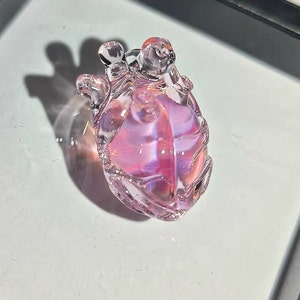 May include: A small, pink glass heart-shaped ornament with a detailed, textured surface.