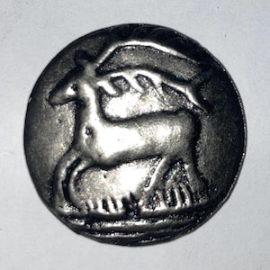 May include: A silver coin with a raised image of a deer with antlers. The deer is facing right and has a detailed design.